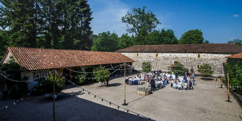 Elevated view of 50 guests at round tables with globe fairy lights in stone farmhouse courtyard