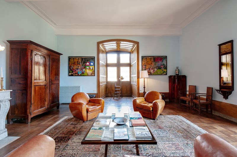 Grand salon with leather club chairs, herringbone parquet, Persian rug, and contemporary art on blue-grey walls