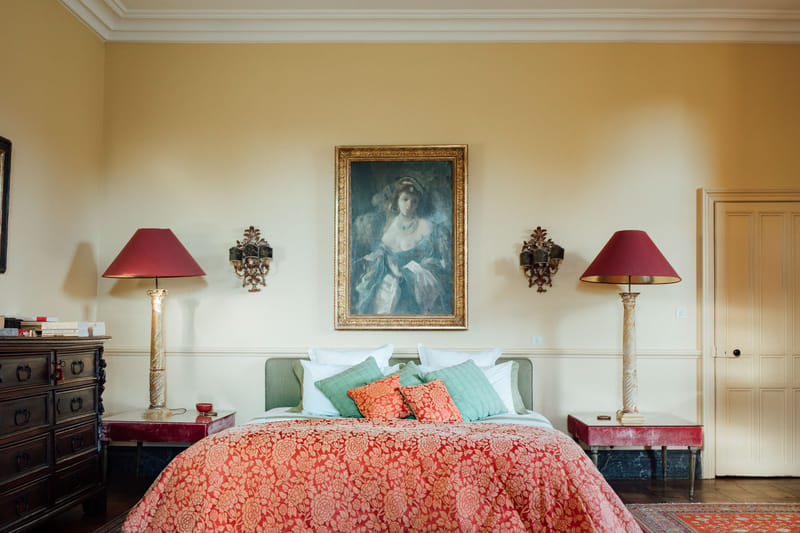 Chateau bedroom with red damask bedspread green headboard gilt portrait Persian rug and wrought iron chandelier