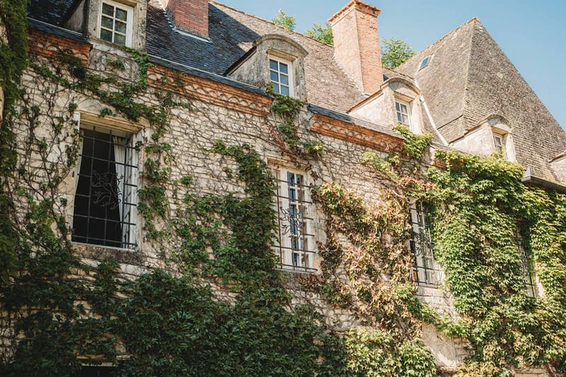 Limestone and brick manor with slate roofs, wrought-iron grilles, and dense climbing ivy facade