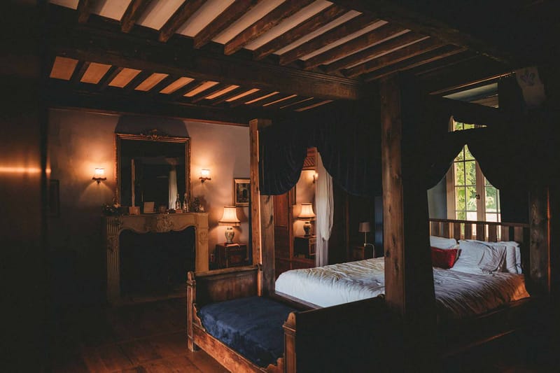 Chateau bedroom with four-poster navy canopy bed, stone fireplace, exposed beams, and amber wall sconces