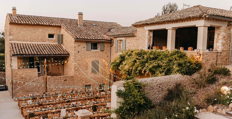 Aerial view of outdoor reception courtyard at Provencal stone farmhouse with long tables and festoon lighting at dusk
