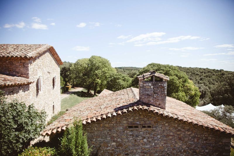 Elevated rooftop view of rustic stone mas buildings with terracotta barrel-tile roofs amid woodland