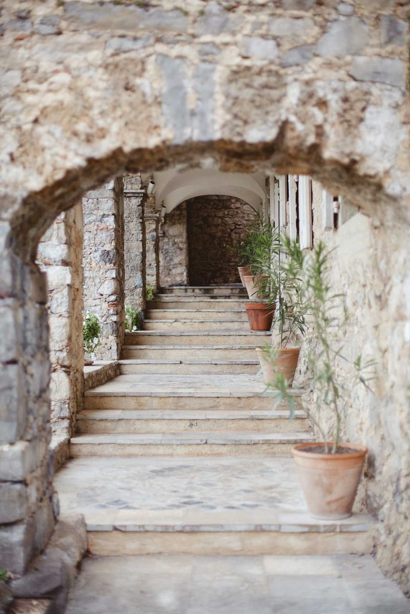 Stone staircases through successive arched passageways with terracotta pots and mosaic-tiled landings