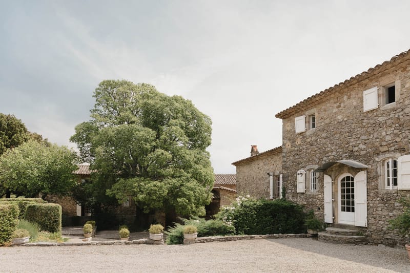 Provencal stone mas with terracotta roofs, white shutters, and gravel courtyard with clipped hedges
