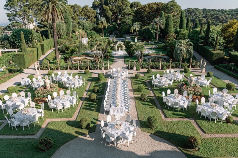 Aerial view of outdoor wedding reception with long head table and round guest tables in formal French garden