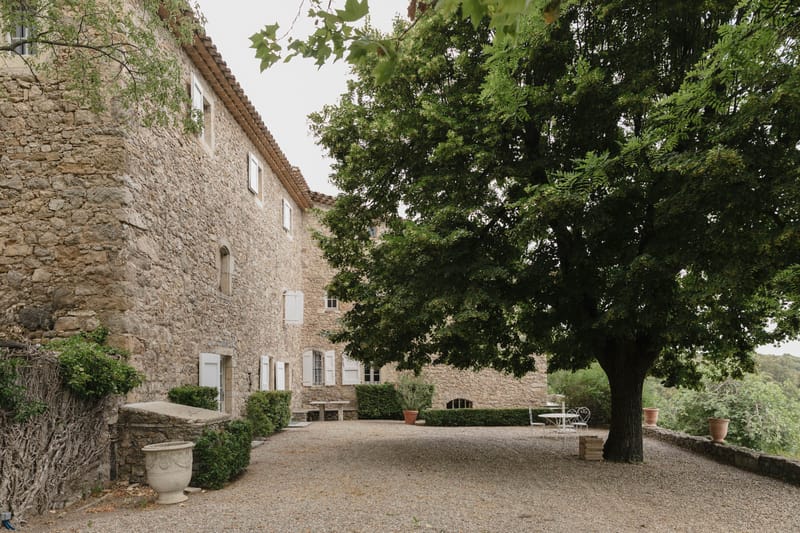Provencal stone mas exterior with golden limestone walls, white shutters, terracotta roof, and gravel courtyard