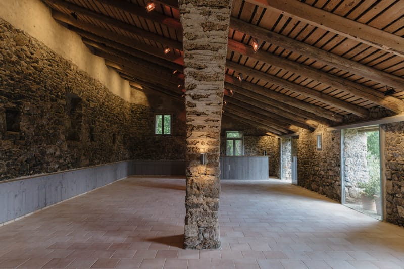 Empty rustic stone event space with wooden beams, terracotta herringbone floor, and built-in bar counter
