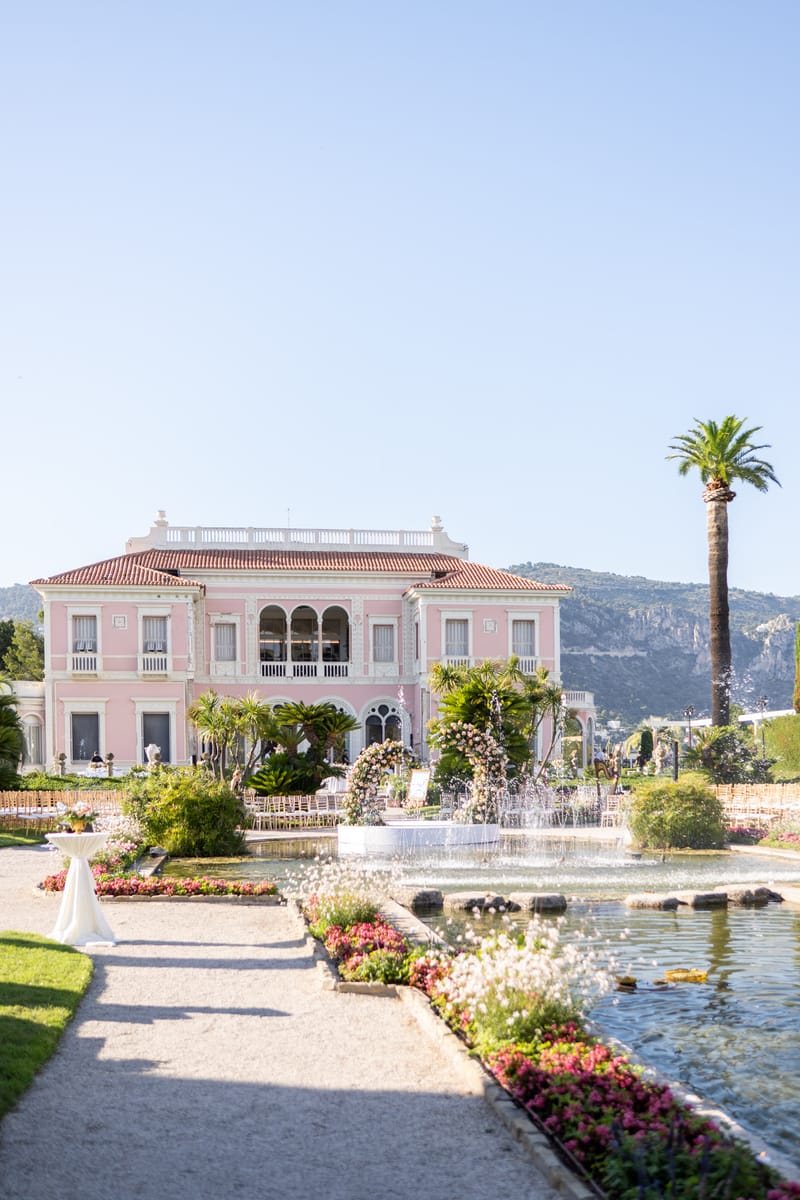 Villa Ephrussi de Rothschild ceremony setup with floral arch near fountain in formal gardens of pink Belle Epoque villa