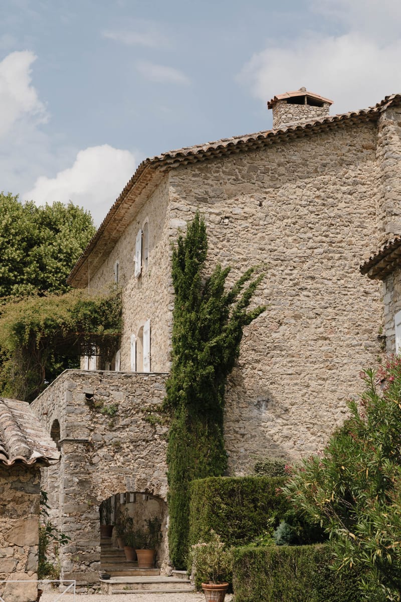 Stone mas facade with terracotta roof tiles, white-shuttered arched windows, cypress trees and boxwood hedging