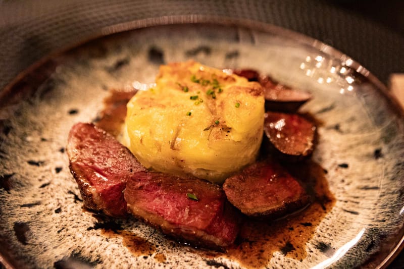 Plated wedding dinner course with sliced red meat and golden potato gratin on speckled ceramic plate with copper rim