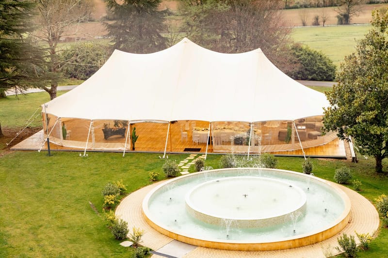 Aerial view of stretch tent reception setup on wooden deck behind a tiered fountain on estate grounds