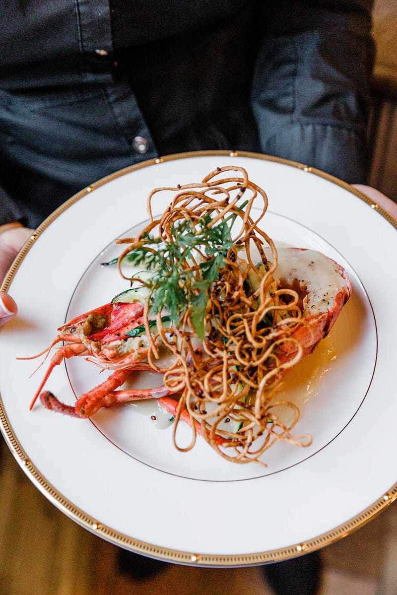 Plated lobster dish with crispy shallots and golden sauce on white plate with gold beaded rim at wedding reception