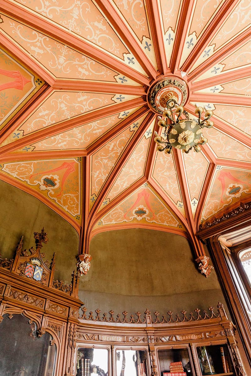 Fan-vaulted ceiling with terracotta ribbing, heraldic shields, and Gothic carved wood paneling inside Chateau Challain