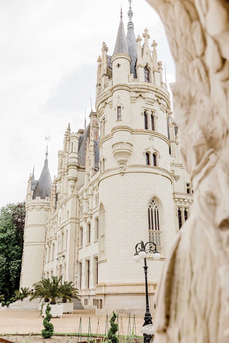 Gothic Revival French chateau with pointed turrets slate roofs arched windows and trimmed topiaries along gravel path