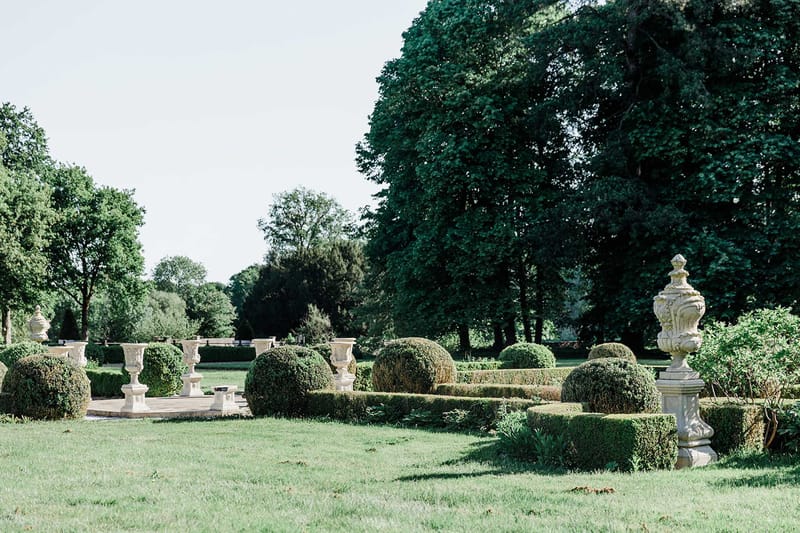 Formal French garden with symmetrical boxwood hedges, stone urns on pedestals, and geometric pathways