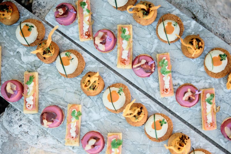 Canape spread of cream tartlets with orange drizzle and pink mousse rectangles on marble surface