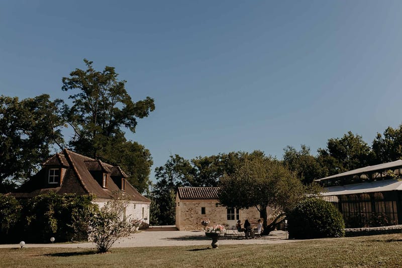 Garden view of stone farmhouse buildings and glass orangery at Domaine de la Fauconnie