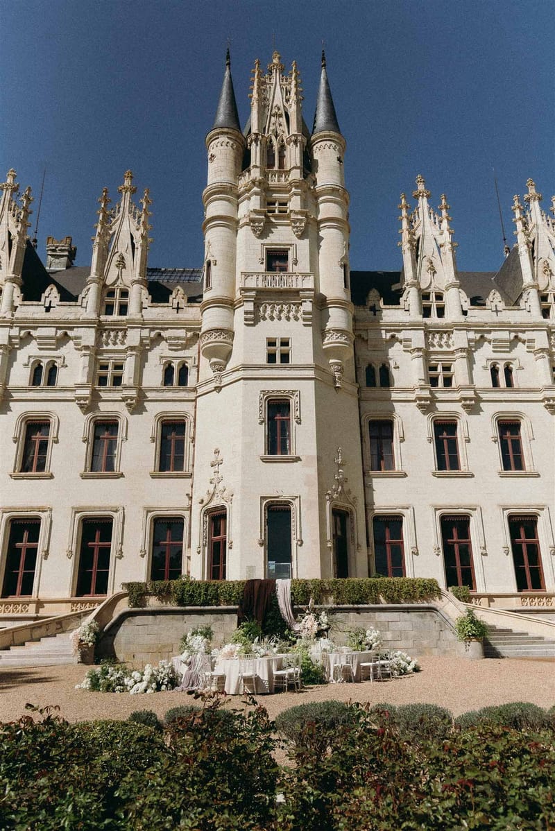 Gothic chateau with limestone facade and slate turrets with reception table and floral arrangements in courtyard