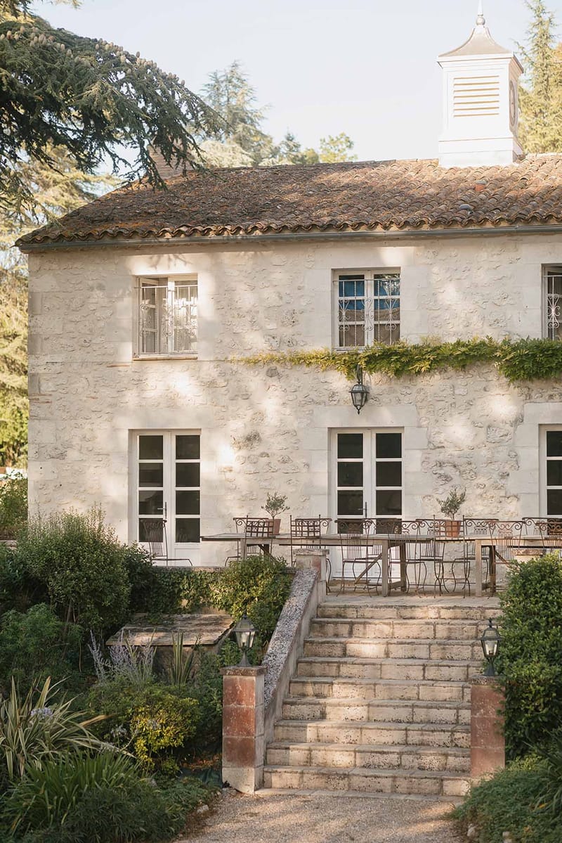 French country manor with cream limestone walls, terracotta roof, and stone staircase leading to furnished terrace
