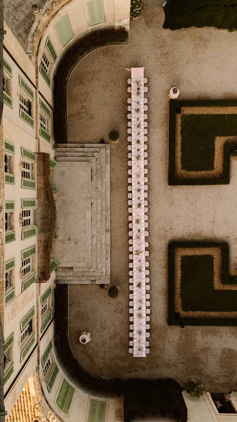 Aerial view of long banquet table in chateau courtyard with parterre gardens and stone facade