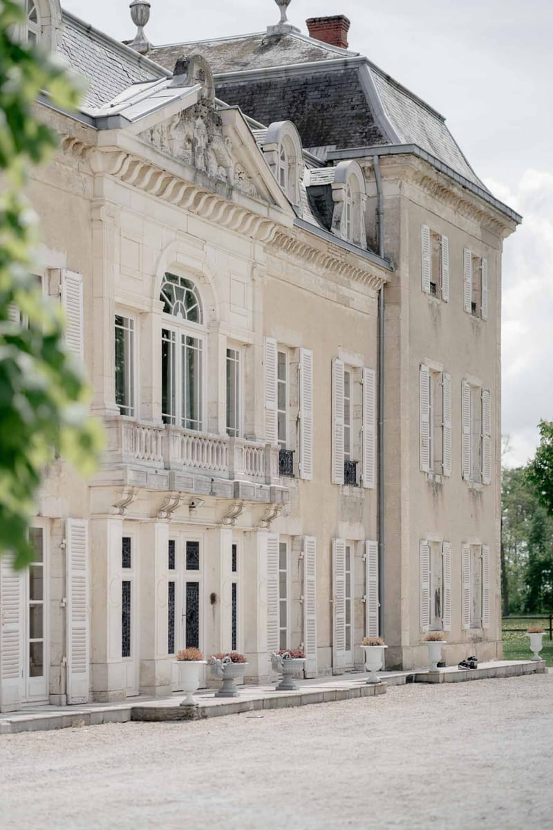 Cream stone French chateau exterior with white shutters mansard slate roof and gravel courtyard