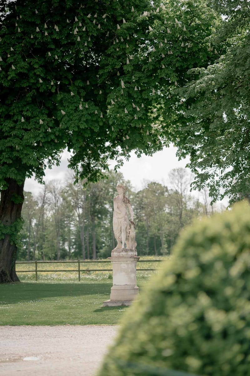 Weathered classical stone statue on pedestal along gravel pathway at French chateau grounds