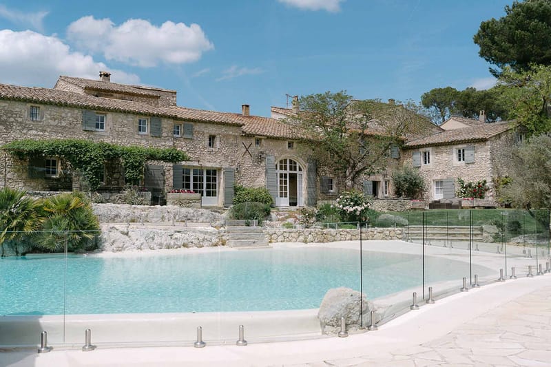 Provencal stone mas with terracotta roofs and grey shutters overlooking rectangular pool and terraced garden