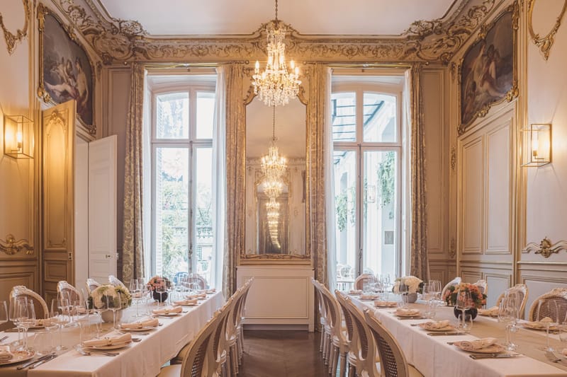 Parallel tables with blush rose centerpieces and gilt cane-back chairs in rococo salon with chandelier