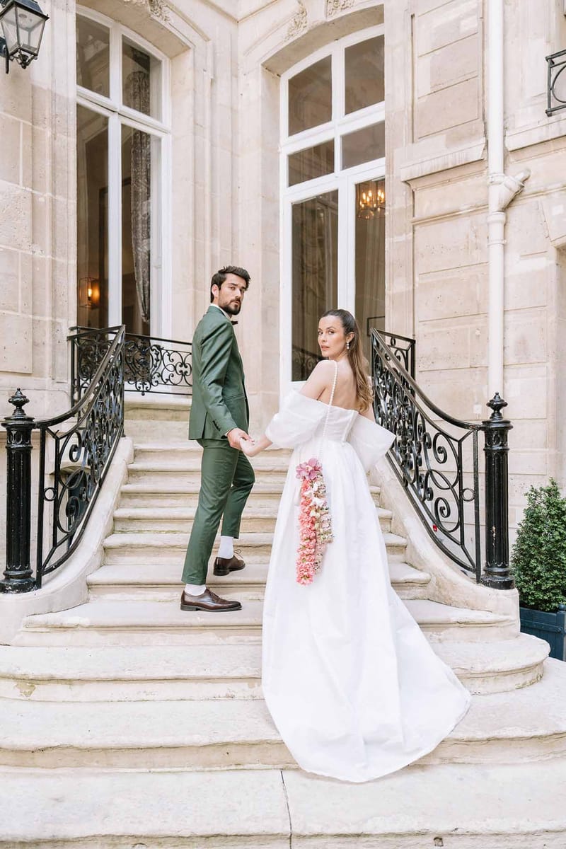 Groom in green suit and bride in off-shoulder ballgown with floral train posing on stone staircase