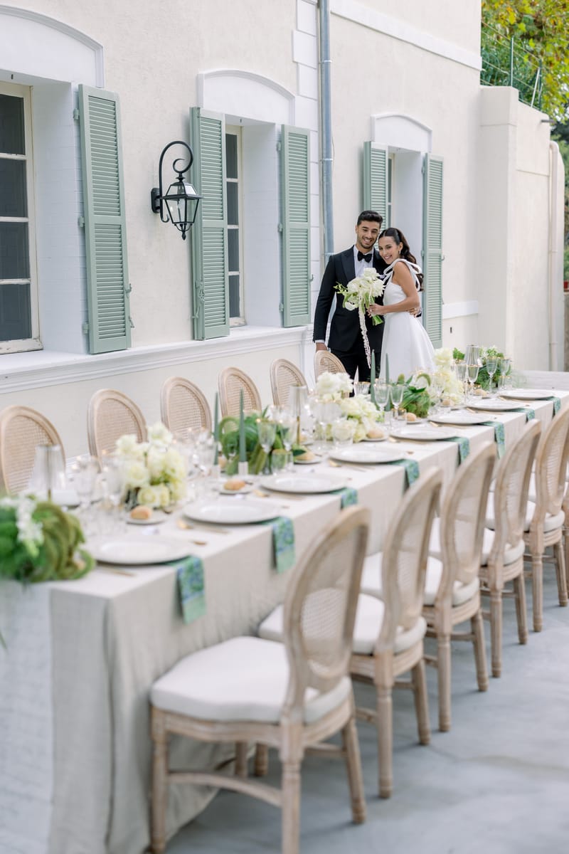 Bride and groom at the end of an outdoor reception table with hydrangea centerpieces and gold candles