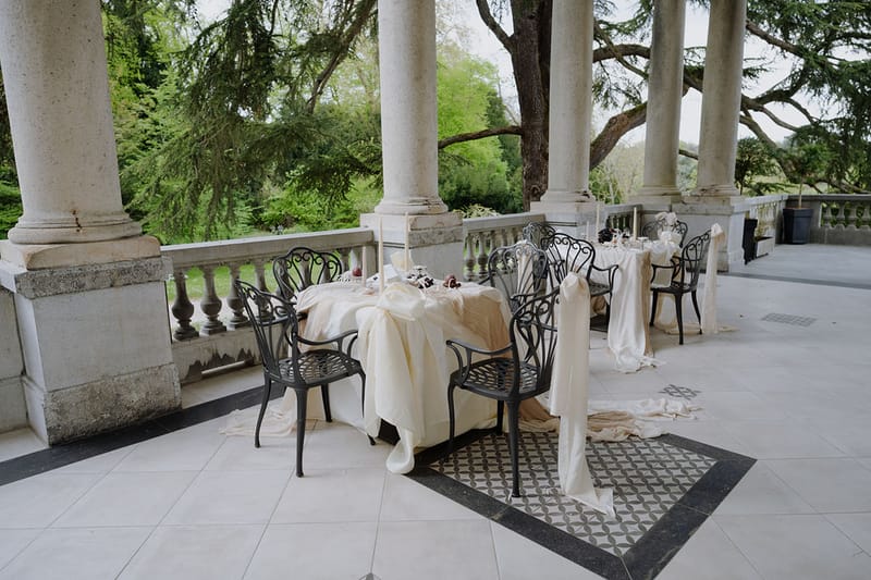 Colonnaded terrace with cream-draped tables, wrought-iron chairs, and geometric tile floor at estate