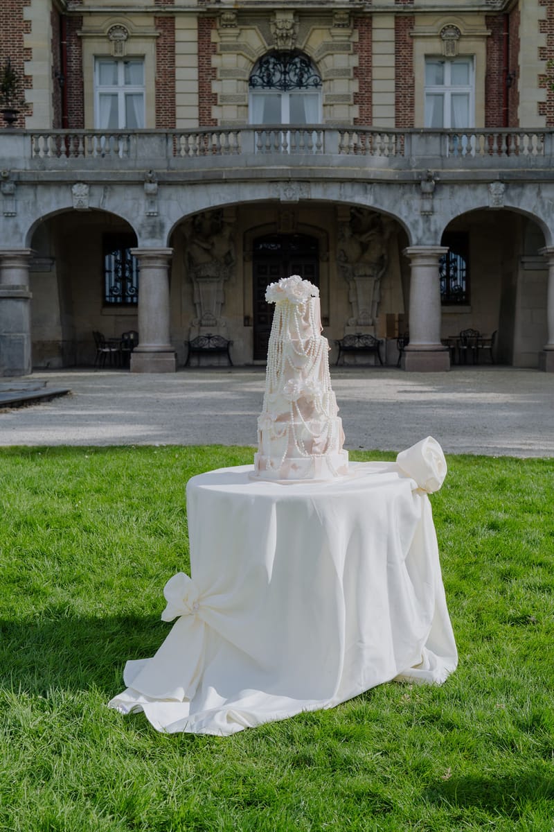 Multi-tiered blush cake with pearl draping and sugar butterflies before red brick chateau colonnade