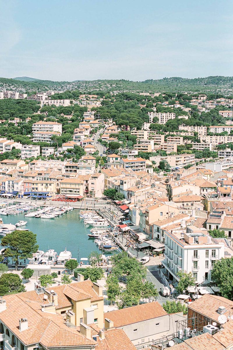 Aerial view of Cassis harbor with sailboats, terracotta-roofed buildings, and waterfront restaurants