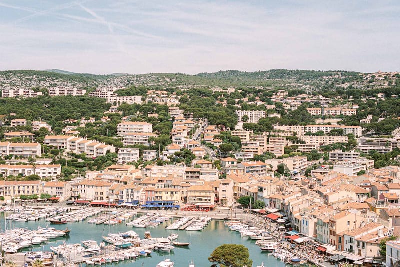 Aerial view of Cassis marina with white sailboats terracotta rooftops and rocky hillside coastline