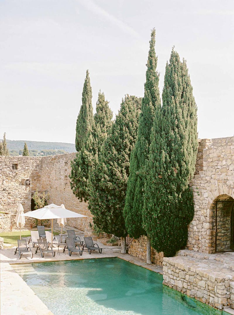 Rectangular pool with turquoise water flanked by sun loungers and cypress trees at Provencal stone venue