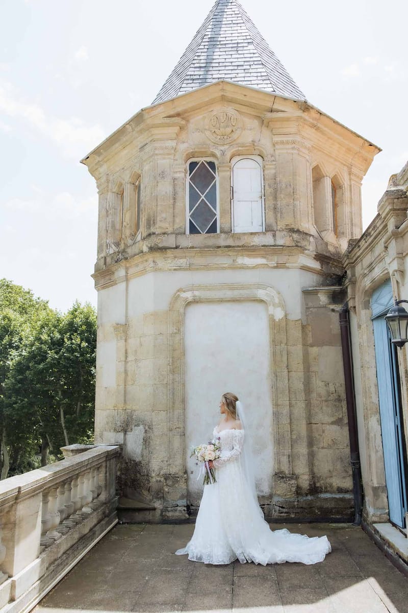 Bride in off-shoulder lace gown with cathedral train and veil on stone terrace of chateau tower