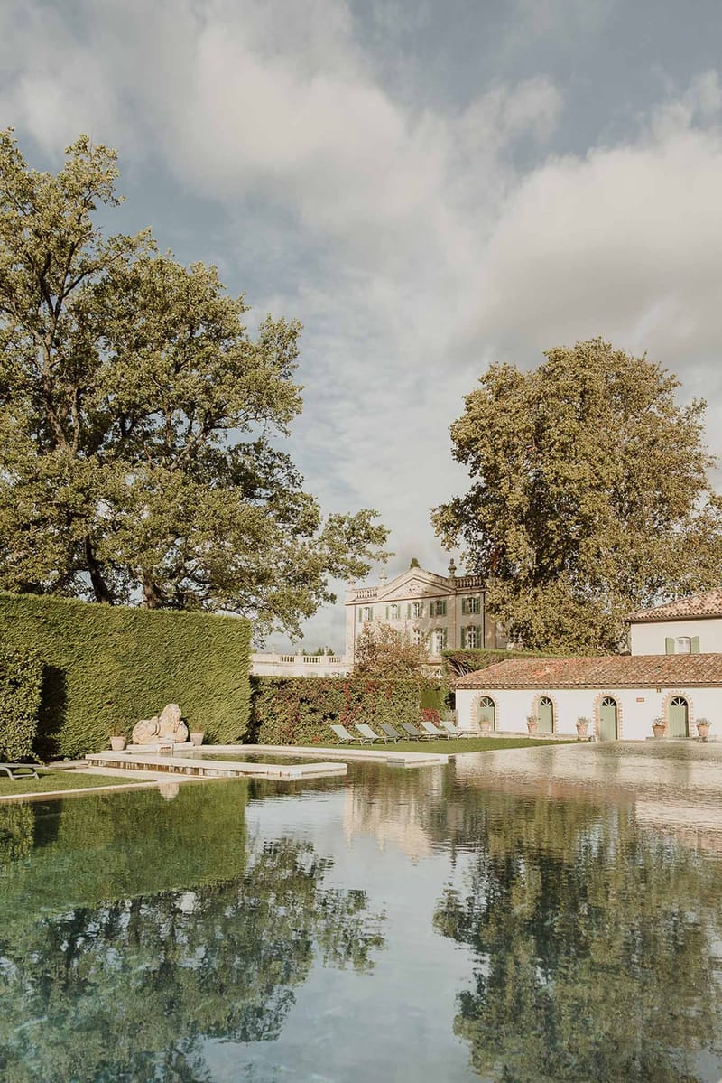 French chateau estate with rectangular reflecting pool, sun loungers, clipped hedges, and stone lion sculptures