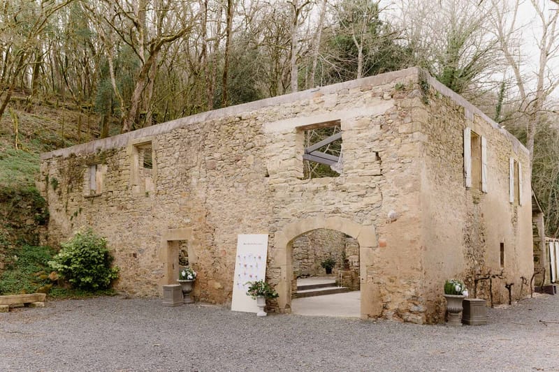 Rustic stone wedding venue entrance with arched doorway, seating chart sign, and potted flowers