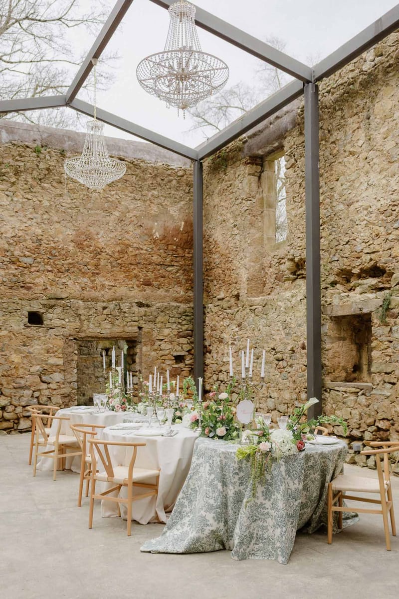 Long reception table in glass-roofed stone ruin with crystal chandeliers, silver candelabras, and blush florals