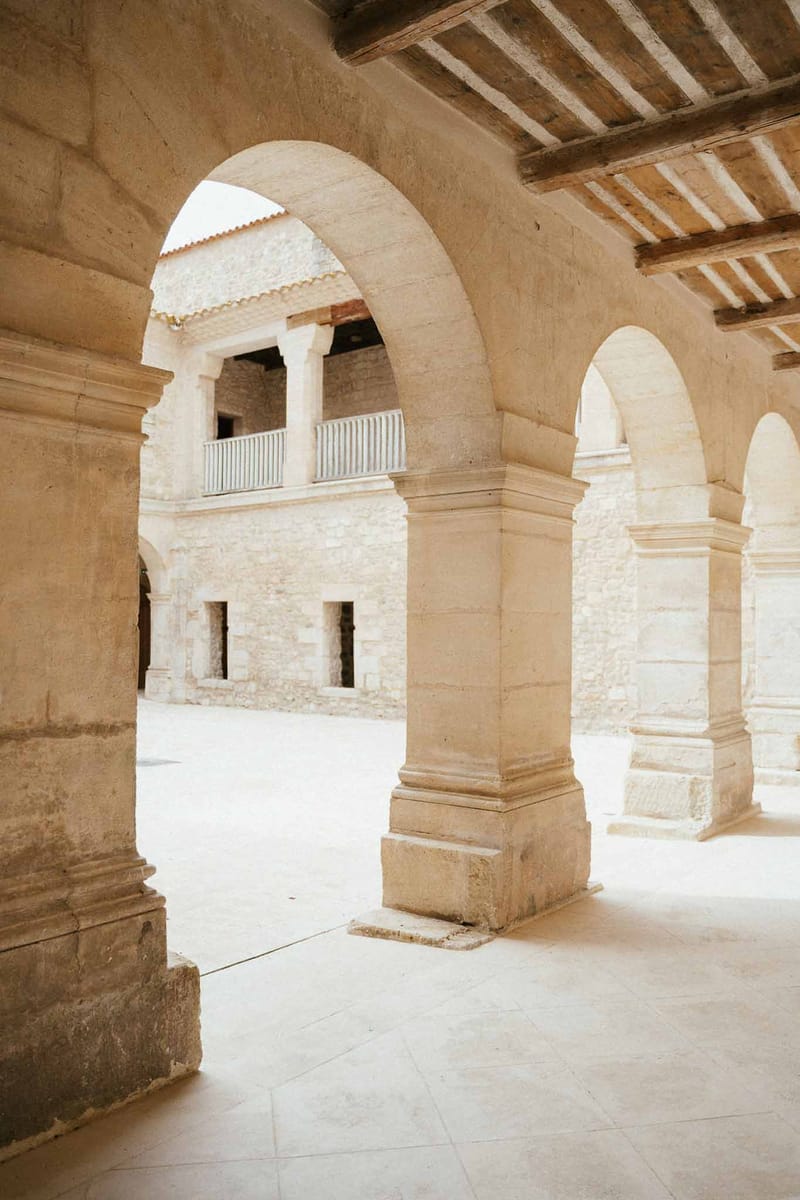 Stone cloister arcade with rounded arches framing two-storey courtyard with upper colonnade and balustrade