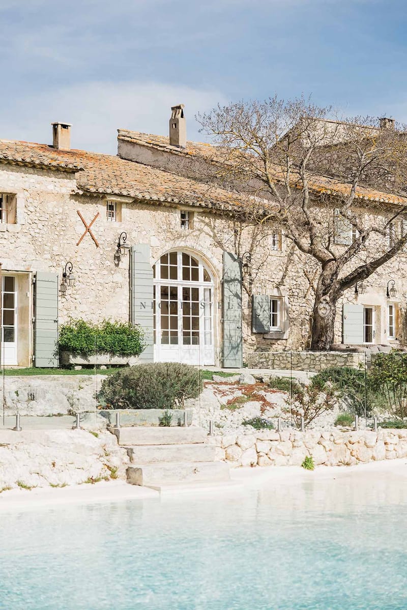 Provencal stone mas with sage shutters, arched French doors, and glass pool fence on limestone terrace