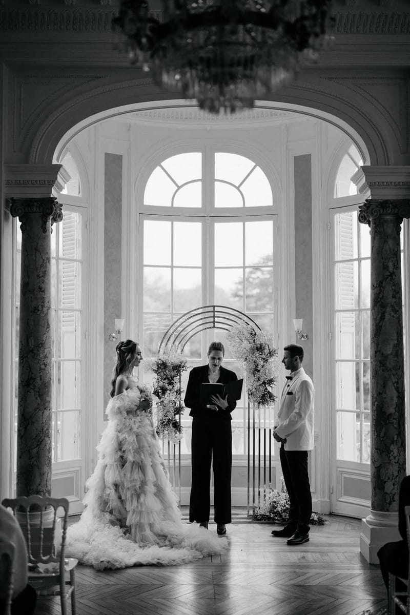 Black and white ceremony in ballroom with ruffled tulle gown, gypsophila circle arch, and herringbone parquet floor