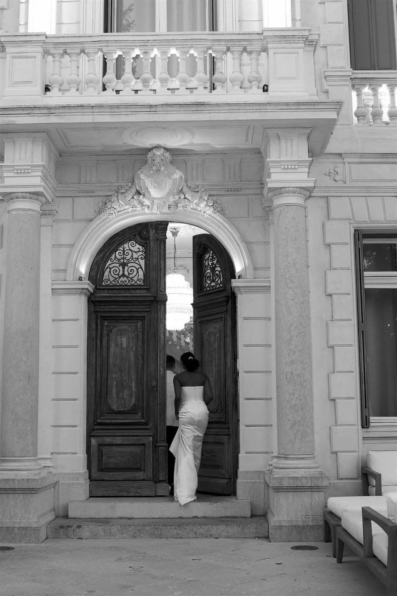 Black and white shot of bride and groom entering grand Baroque building through ornate double wooden doors