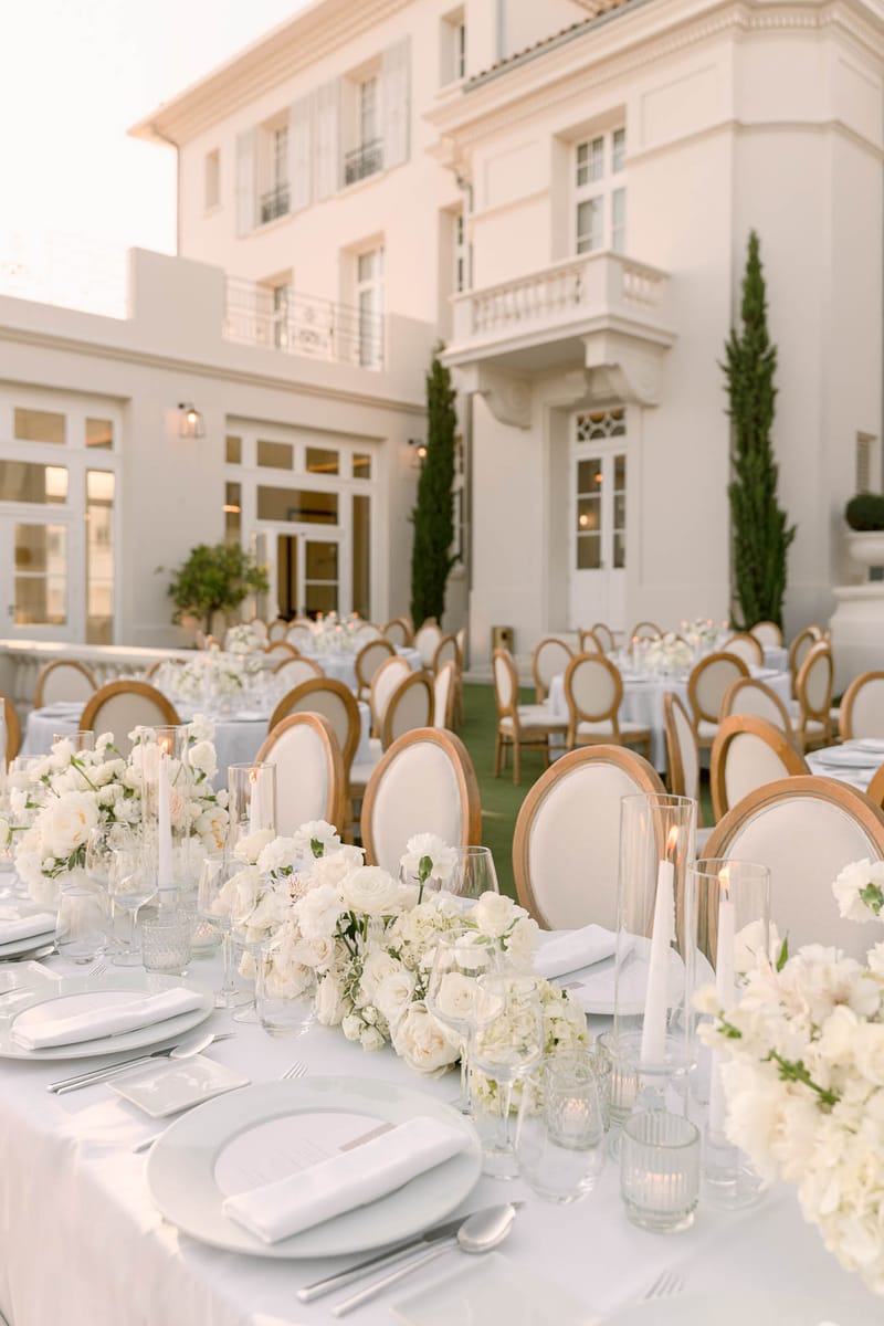 White rose and hydrangea table with gold oval-back chairs before white villa facade at dusk