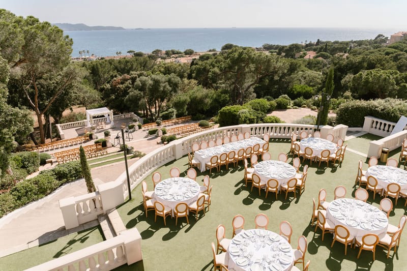 Aerial view of terraced Mediterranean venue with round reception tables, ceremony pergola, and sea beyond