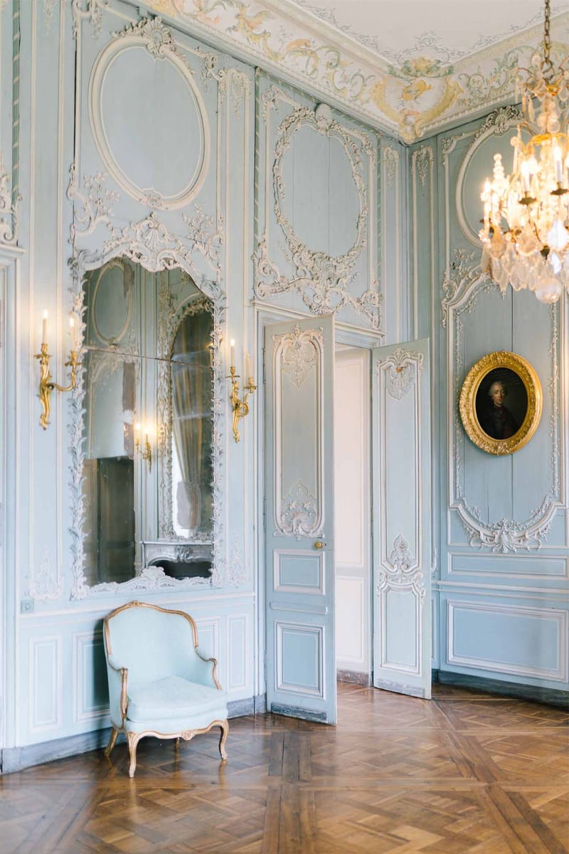 Powder-blue Rococo salon with white boiserie, gilt mirror, crystal chandelier, and herringbone parquet floor