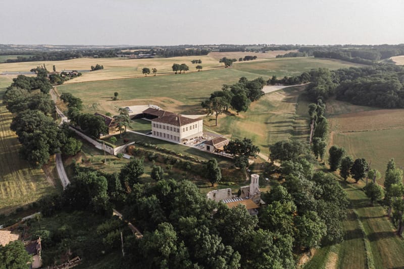 Aerial drone view of French country estate with manor house, barn, and surrounding fields