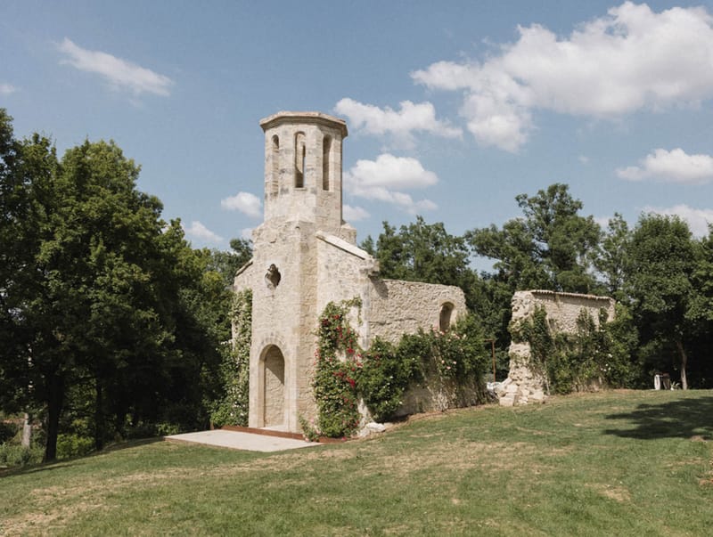 Romanesque stone chapel with octagonal bell tower and climbing roses on grassy hillside