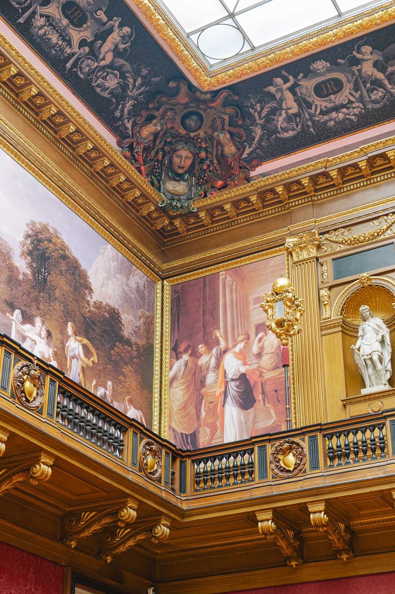 Ornate Belle Epoque interior with gilded balcony, classical paintings, cherub cornice, and glass skylight